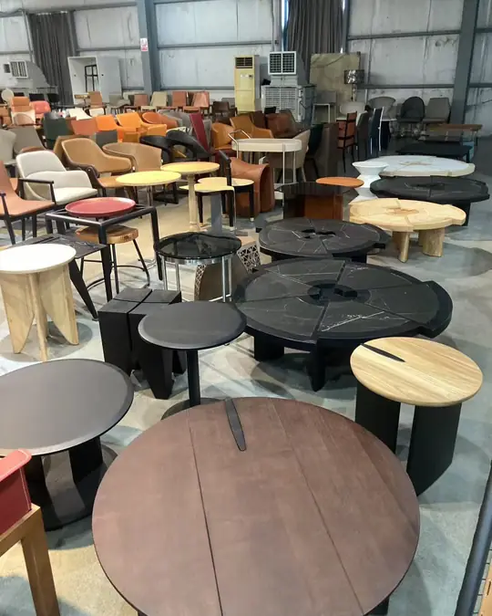 Round and oval coffee tables in dark stained timber and black metal grouped across a showroom floor, with armchairs behind