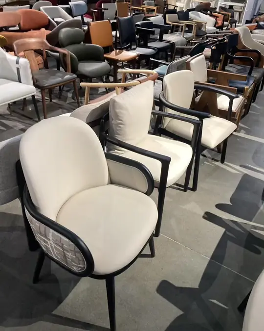 Cream and grey upholstered lounge armchairs with black frames, sunlight casting hard shadows across the showroom floor