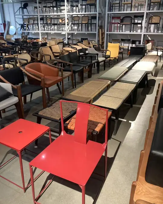 Two bright red powder-coated steel chairs beside a long wooden bench, with rows of wooden chairs and tables behind