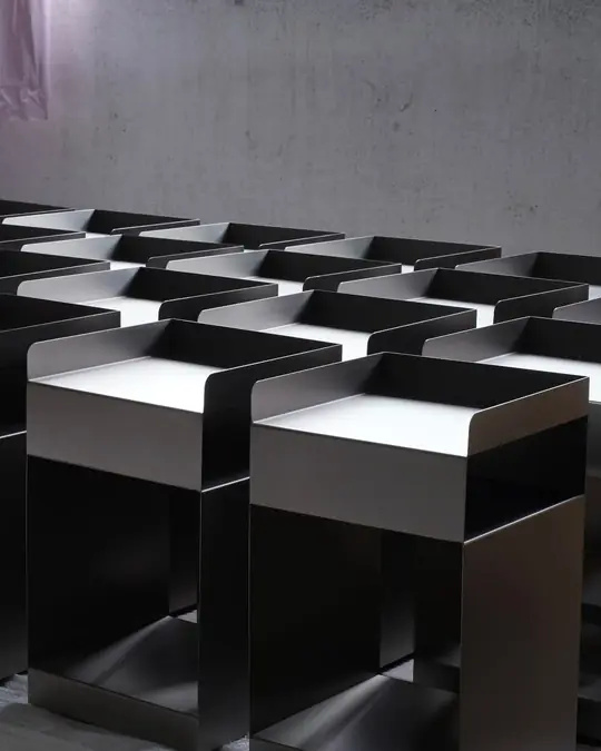 Rows of nested grey metal side tables stacked on a warehouse floor